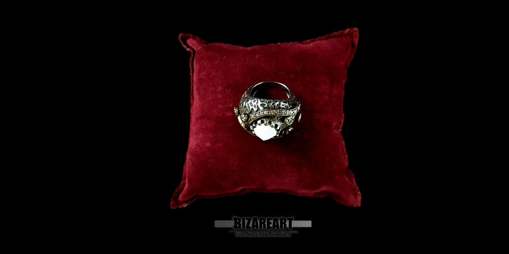 Overhead view of an intricate white agate claw-set ring displayed on a plush red velvet jewelry pillow.