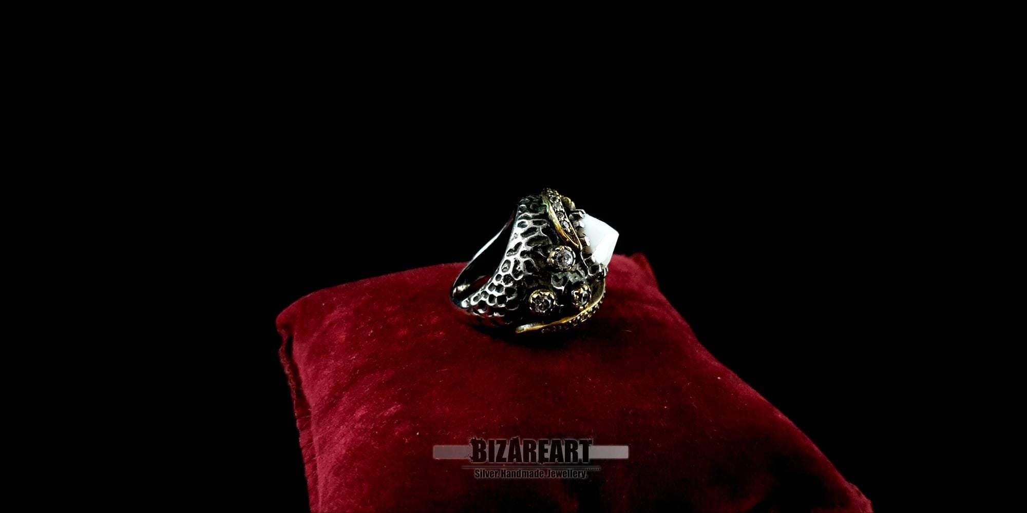 Side profile of the textured, oxidized silver ring band with gold-plated details on a red velvet cushion.
