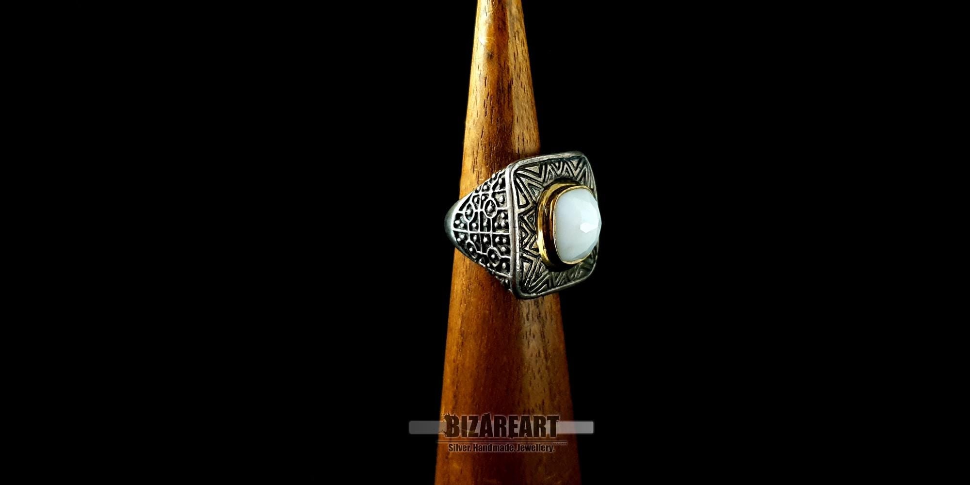 Close-up side view of the artisan silver ring on a wooden display stand, showcasing the intricate traditional engravings along the band.