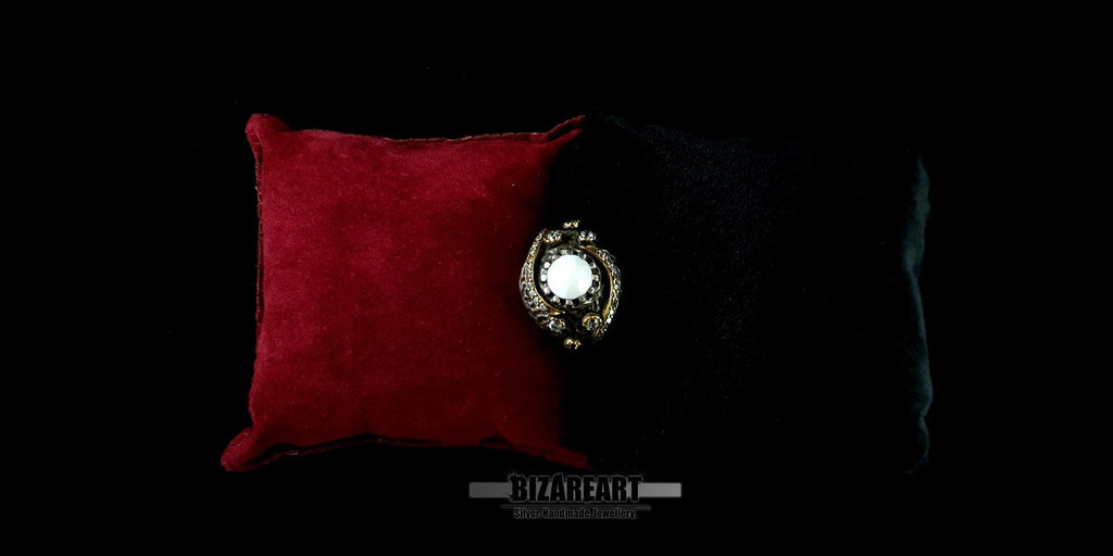 Studio shot of the white agate gemstone ring displayed on a dark background next to a red velvet cushion.