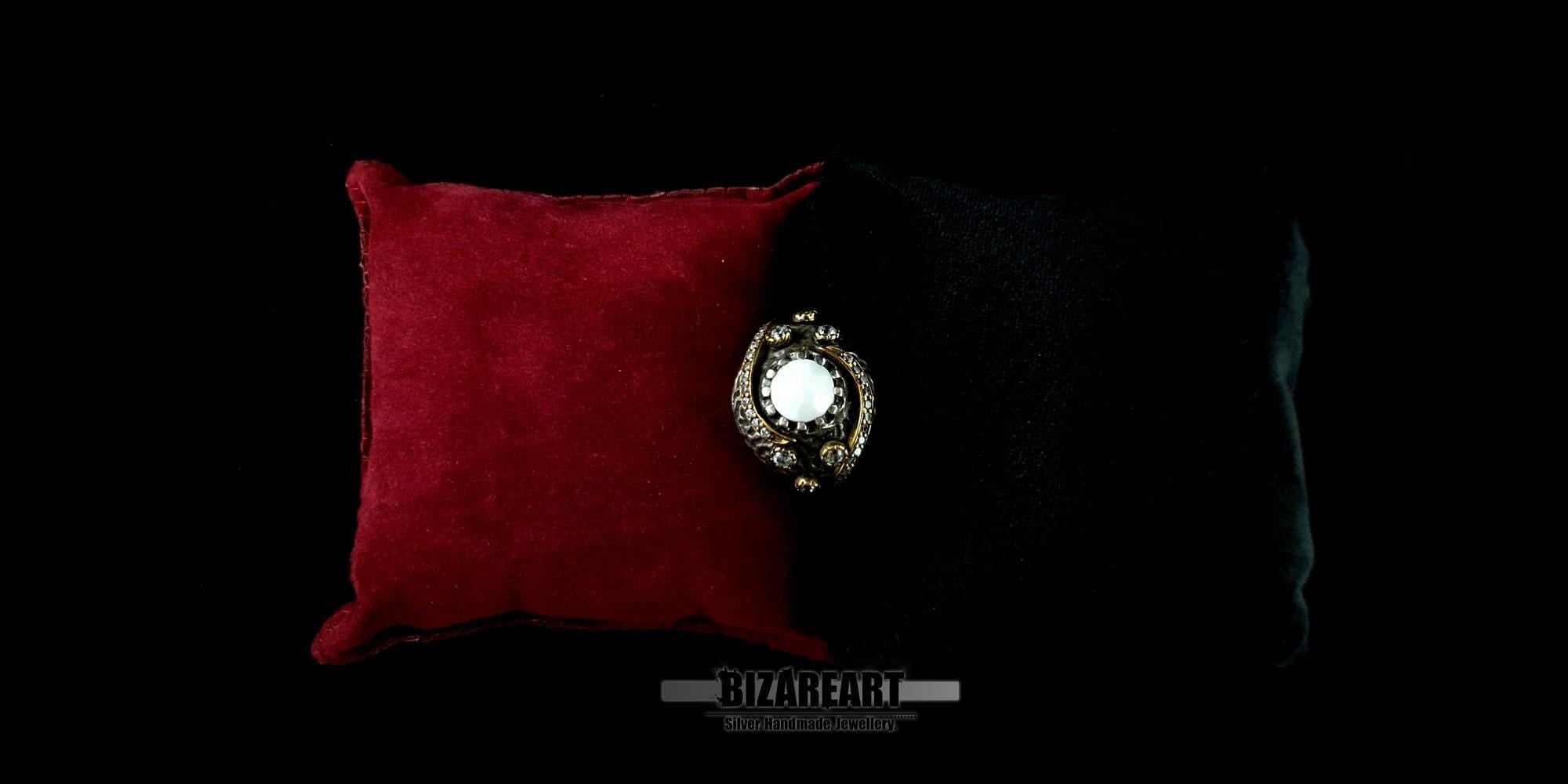 Studio shot of the white agate gemstone ring displayed on a dark background next to a red velvet cushion.