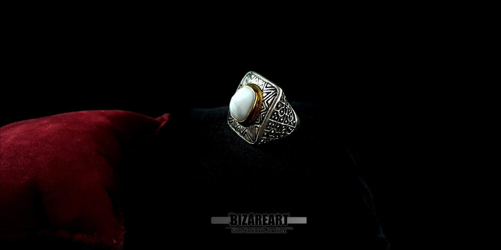 Side profile of an engraved silver ring with a prominent white agate gemstone, showcasing the detailed craftsmanship against a dark backdrop.