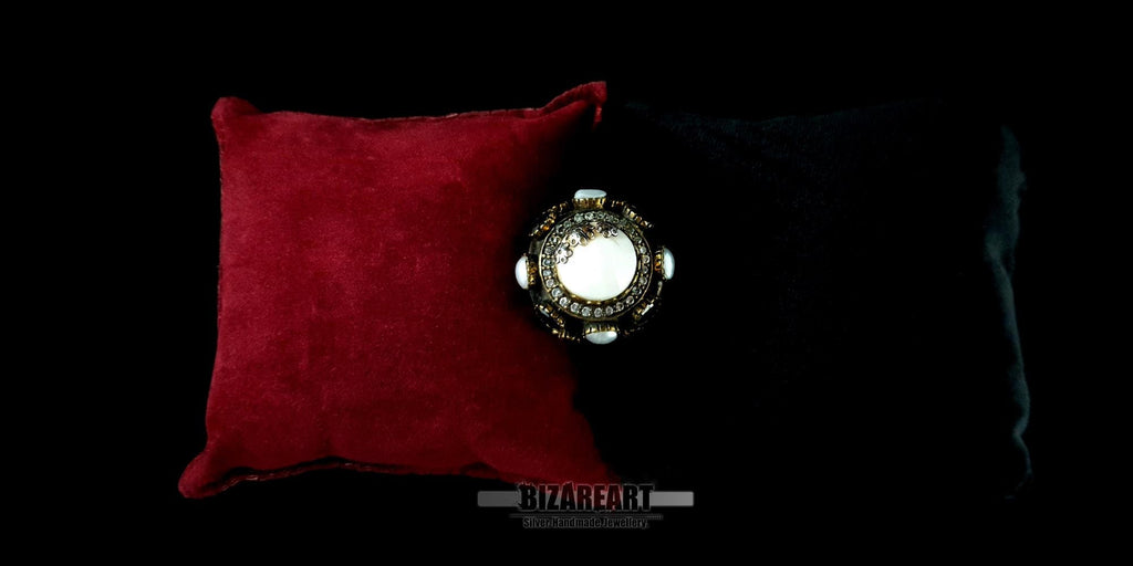 Top view of an oxidized silver gothic dome ring with a central white agate stone on a red cushion.