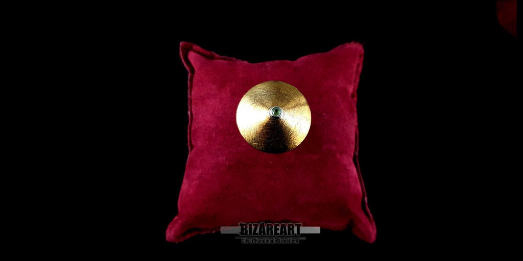 Top-down view of a handcrafted silver and gold-plated cymbal ring with a center peridot gemstone, resting on a plush red velvet cushion.