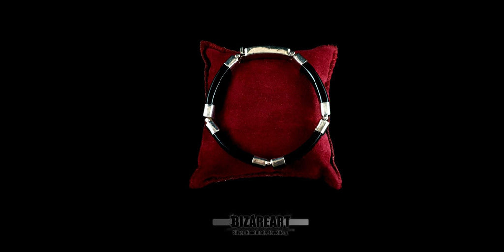A top-down view of a sleek, black onyx bracelet with silver accents resting on a plush red velvet cushion, set against a dark, dramatic background.