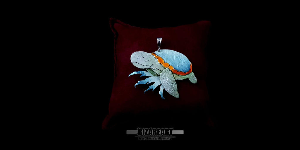 High-contrast studio shot of the artisan silver sea turtle pendant resting on a dark surface, highlighting the detailed hand-engraved flippers and colorful enamel.