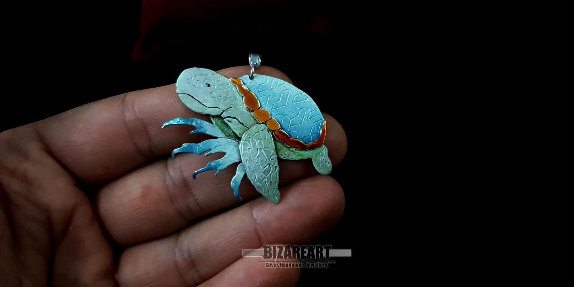 The sterling silver sea turtle pendant held in a hand to demonstrate its 4.5 cm scale and wearable size.