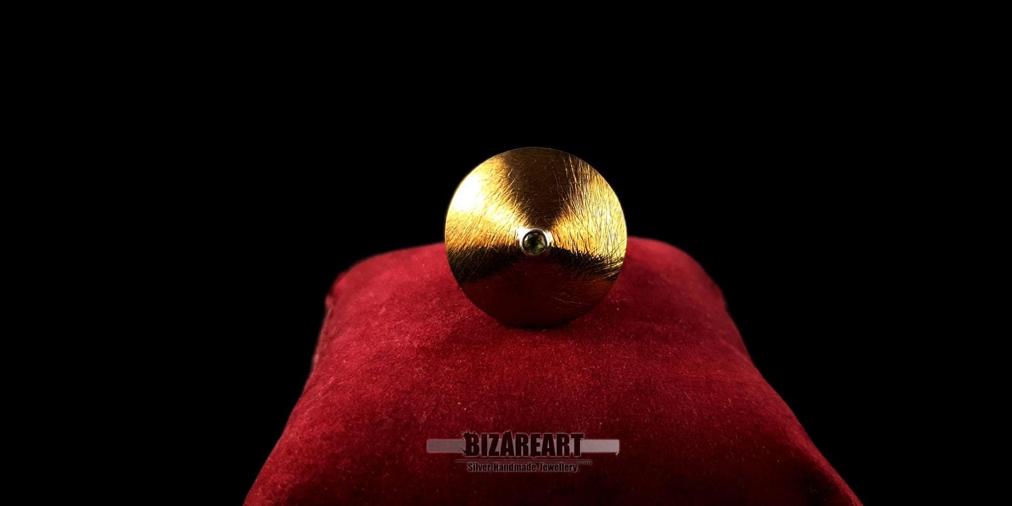 Frontal view of the gold-plated cymbal ring showing the textured metallic surface and center green peridot.