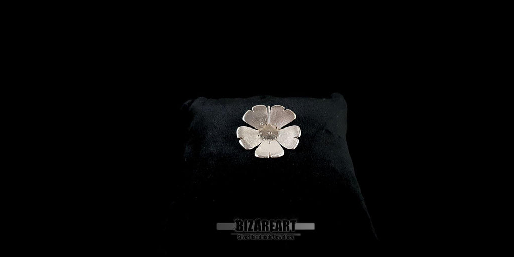 Close-up of the handcrafted silver flower necklace resting on a black display cushion, highlighting its polished and textured finish.