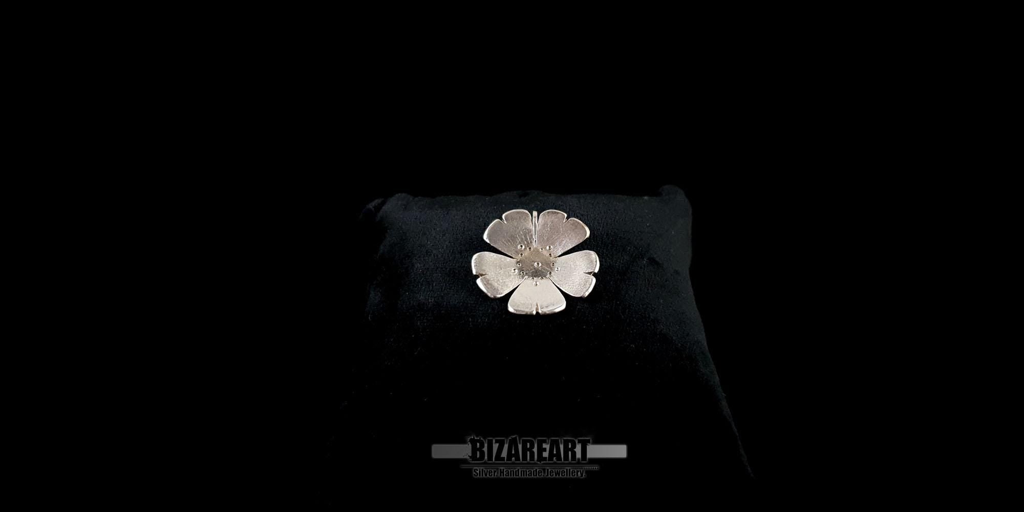 Close-up of the handcrafted silver flower necklace resting on a black display cushion, highlighting its polished and textured finish.