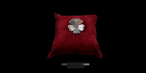 Wide shot of the artisan silver floral pendant centered on a red velvet display pillow with a black background.