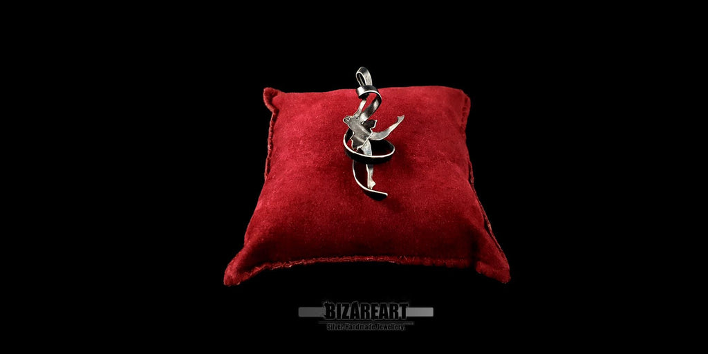 Front view of the oxidized silver ribbon dancer pendant on a red velvet pillow, showcasing the intricate detail and dark patina.