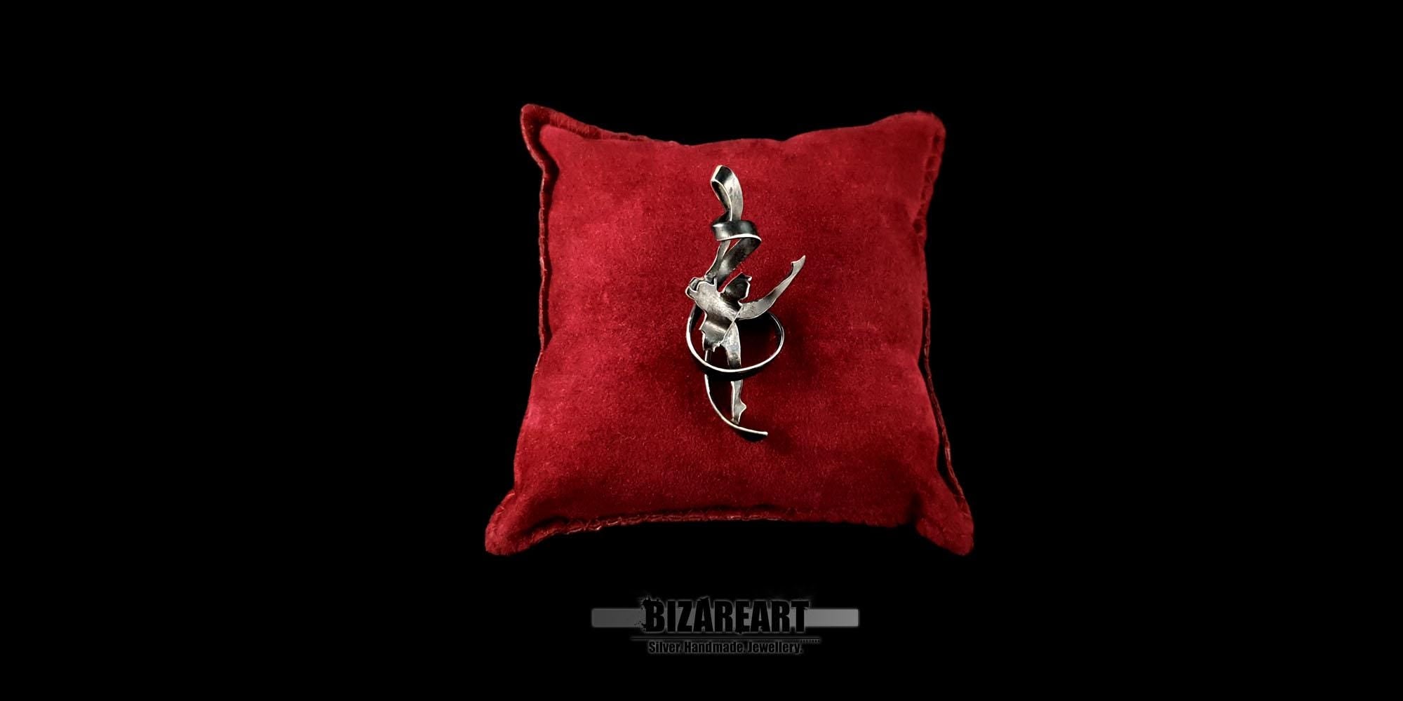 A handcrafted 3D ballet dancer pendant in oxidized silver resting on a plush red velvet cushion against a dramatic black background.