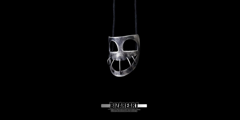 Centered shot of the oxidized silver mask pendant hanging on an adjustable black cord with the Bizareart logo underneath.