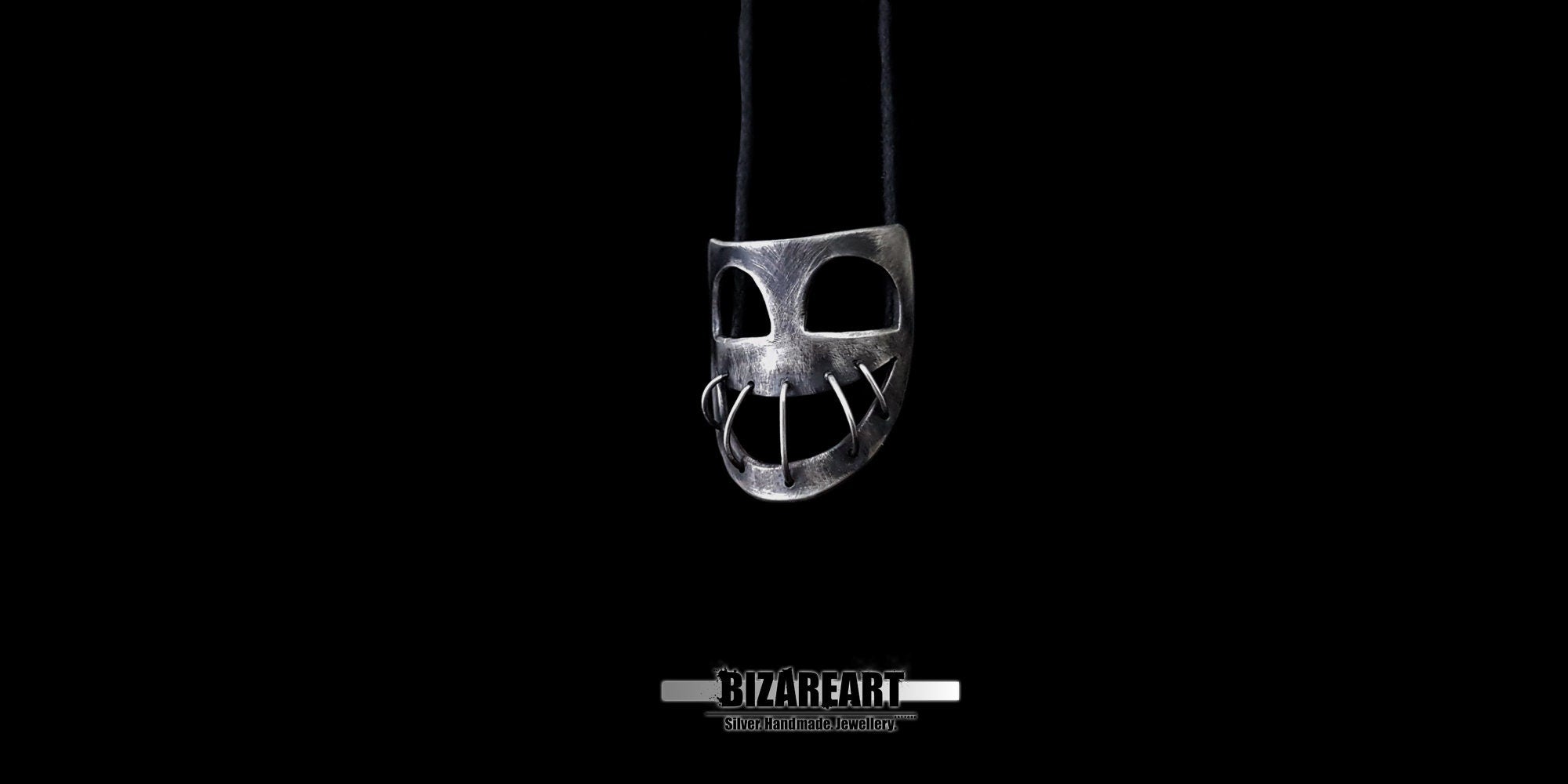 Centered shot of the oxidized silver mask pendant hanging on an adjustable black cord with the Bizareart logo underneath.