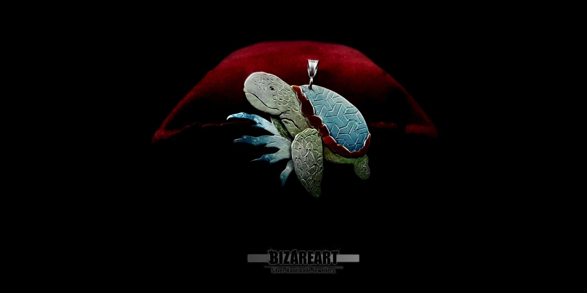 A handcrafted 925 sterling silver sea turtle pendant with a vibrant light blue and orange enamel shell, displayed against a dark background with a red artistic curve.