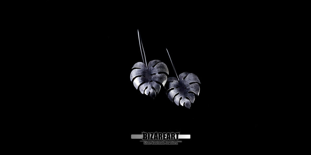 Close-up of silver Monstera leaf earrings showing the unique "bend deformation" and hand-scratched texture for a realistic botanical look.