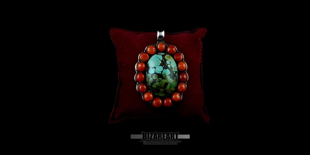 Handmade sterling silver bohemian pendant featuring a large oval green-blue Himalayan turquoise stone surrounded by a halo of round red coral beads, displayed on a dark red velvet pillow.
