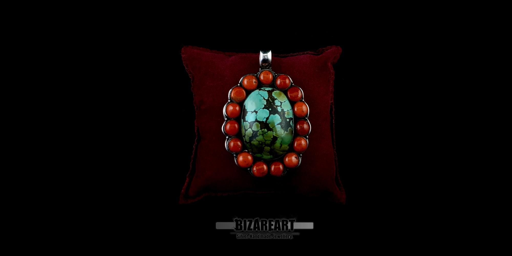Handmade sterling silver bohemian pendant featuring a large oval green-blue Himalayan turquoise stone surrounded by a halo of round red coral beads, displayed on a dark red velvet pillow.