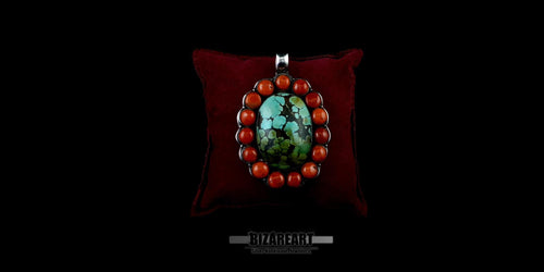 Handmade sterling silver bohemian pendant featuring a large oval green-blue Himalayan turquoise stone surrounded by a halo of round red coral beads, displayed on a dark red velvet pillow.
