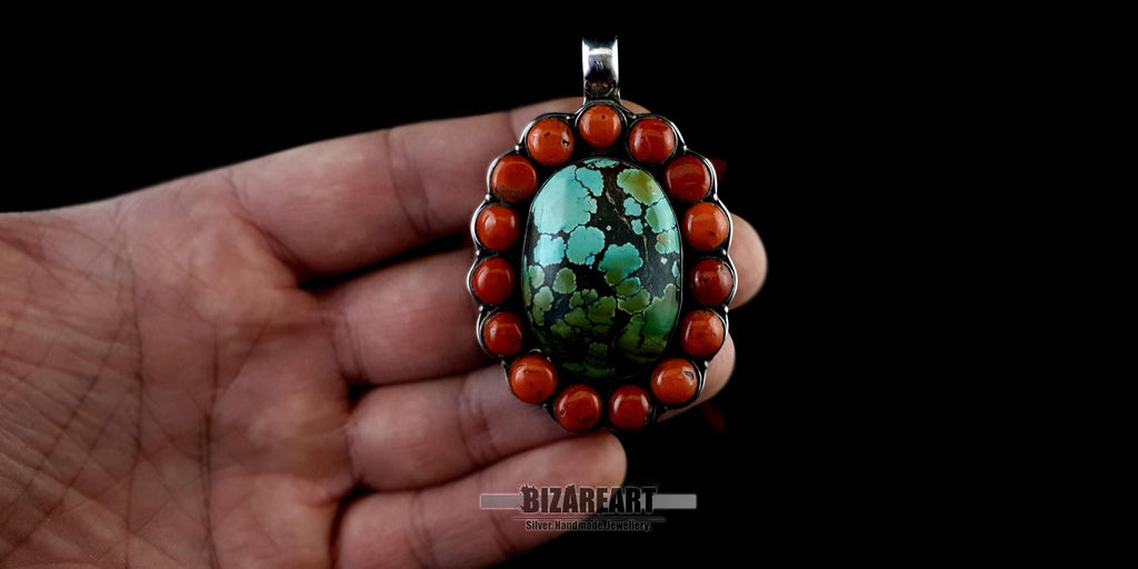 Large Himalayan turquoise and red coral silver pendant held in a person's hand to show the substantial scale, size, and craftsmanship of the jewelry piece.