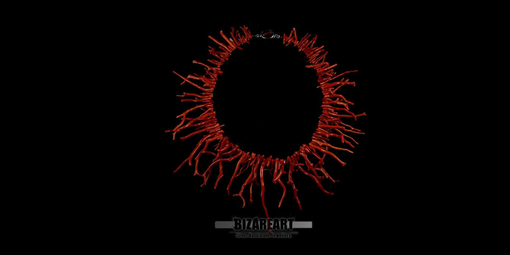 A striking Mediterranean Red Coral necklace displayed against a solid black background. The coral branches radiate outward in a circular pattern, creating a bold, organic fringe.