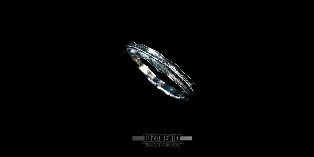 A side profile of the bracelet suspended against a black void, emphasizing the jagged, raw edges and the contrast between the polished silver highlights and deep black oxidation.