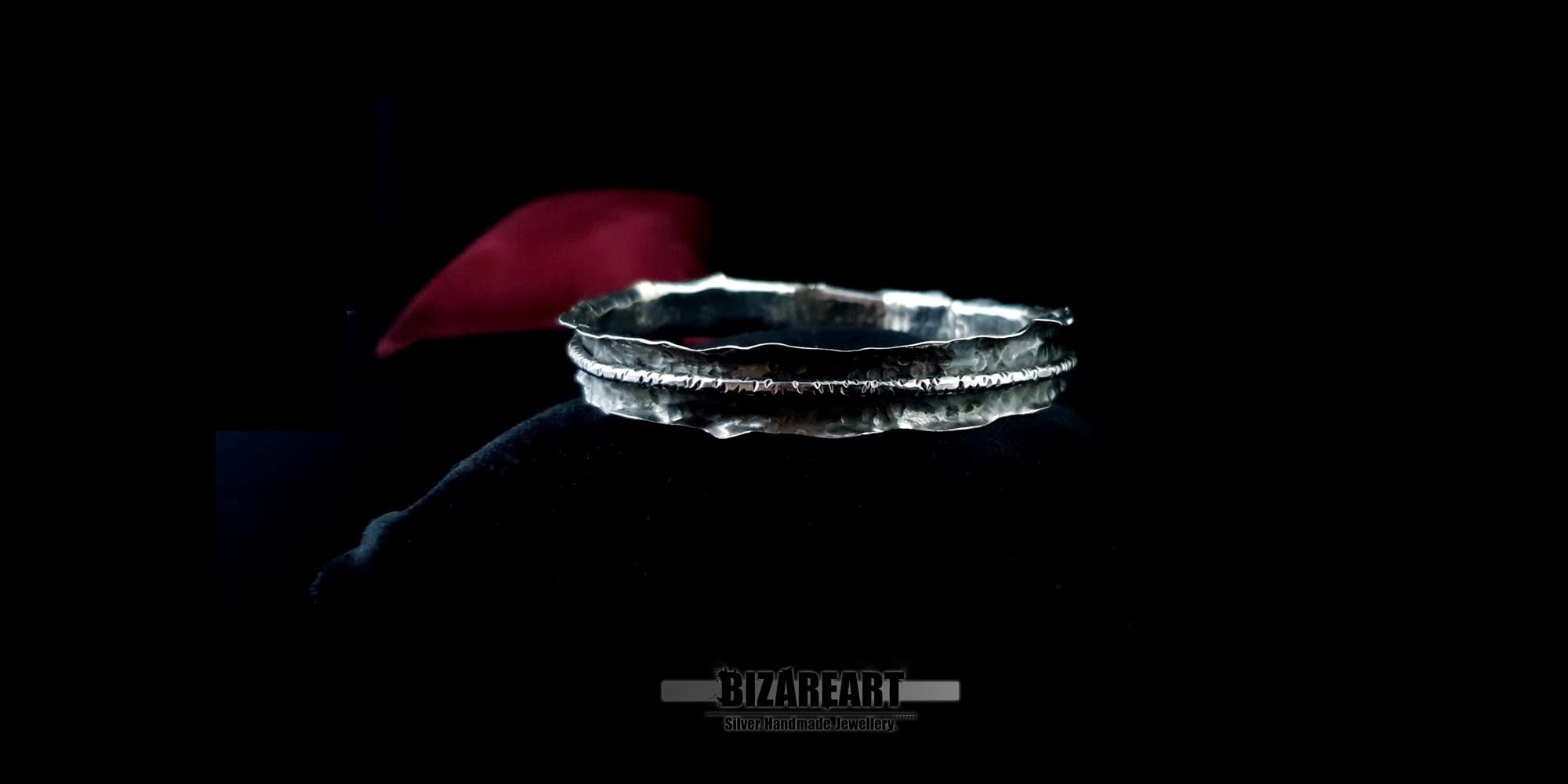 A wide shot of the bracelet on the red velvet cushion, demonstrating how the piece catches the light across its "silver spine" center band.