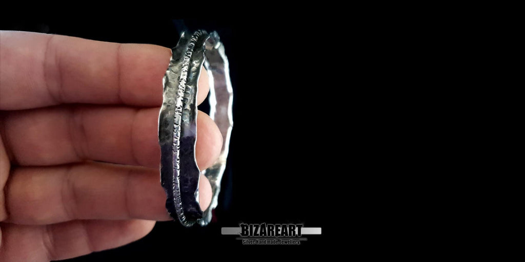A person holding the Bound Contrast Bracelet between their fingers, providing a clear sense of its 17.5g thickness and 7 cm diameter scale.