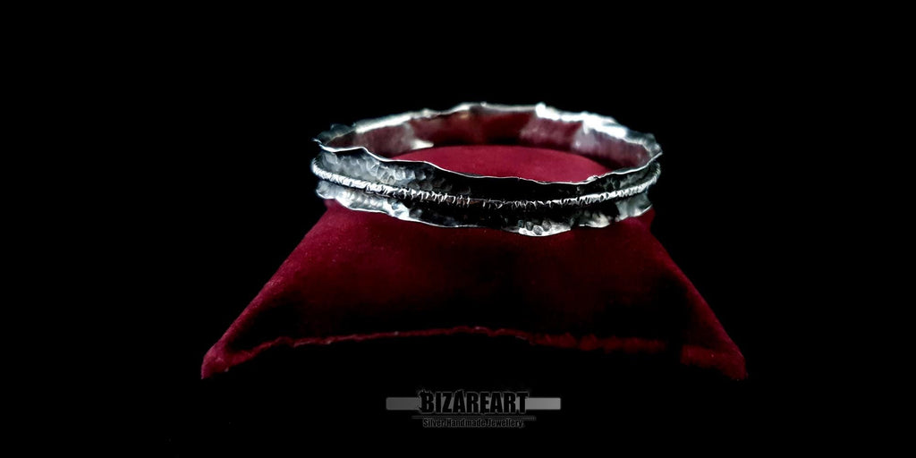 Close-up of the Bound Contrast Bracelet resting on a plush, deep red velvet cushion. The shot highlights the rugged, hand-hammered texture of the sterling silver and the distinct oxidized dark band running through the center.