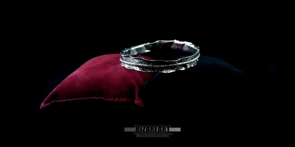 High-angle view of the silver cuff on a dark background, showcasing the asymmetrical, "spontaneously shaped" curvature of the metal.