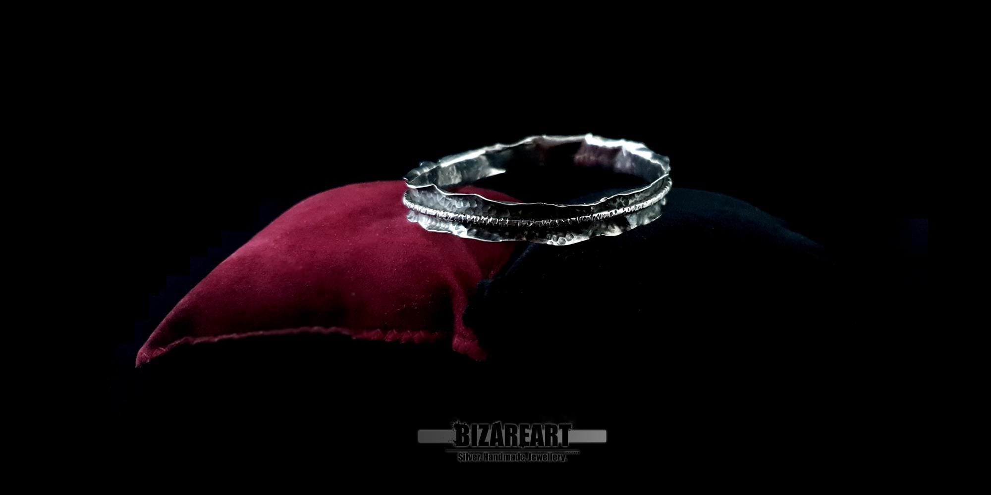 High-angle view of the silver cuff on a dark background, showcasing the asymmetrical, "spontaneously shaped" curvature of the metal.