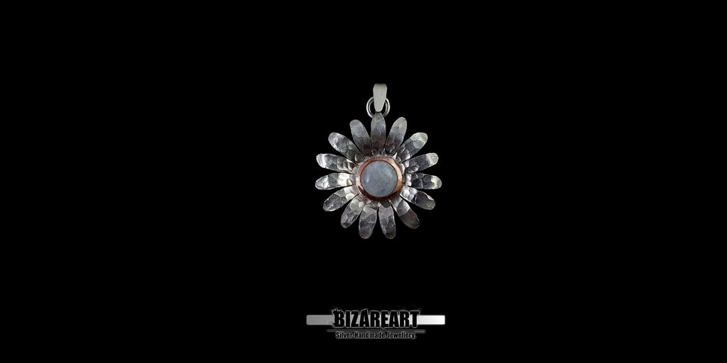 Front view of a handmade textured sterling silver daisy pendant with a luminous round moonstone center and copper bezel, set against a solid black background.