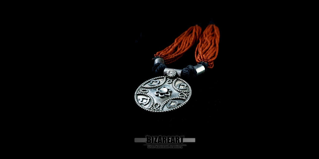 Close-up, angled view of a handmade garnet bead necklace showcasing the layered texture and the antique finish of the silver pendant.
