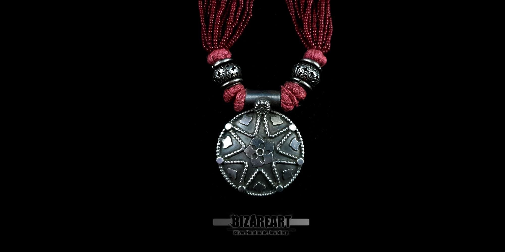 Detailed macro shot of the raised carvings and vintage oxidized finish on the round silver pendant of the red beaded necklace.