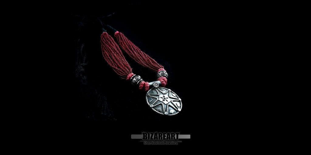 Angled close-up shot showing the hand-wrapped red cotton thread details connecting the multi-strand seed beads to the large silver pendant.