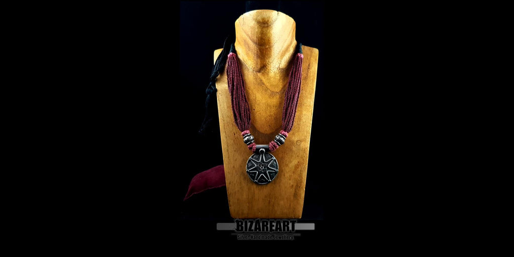 Side-angled view of the adjustable multi-strand red statement necklace on a wooden mannequin display, highlighting its drape and texture.