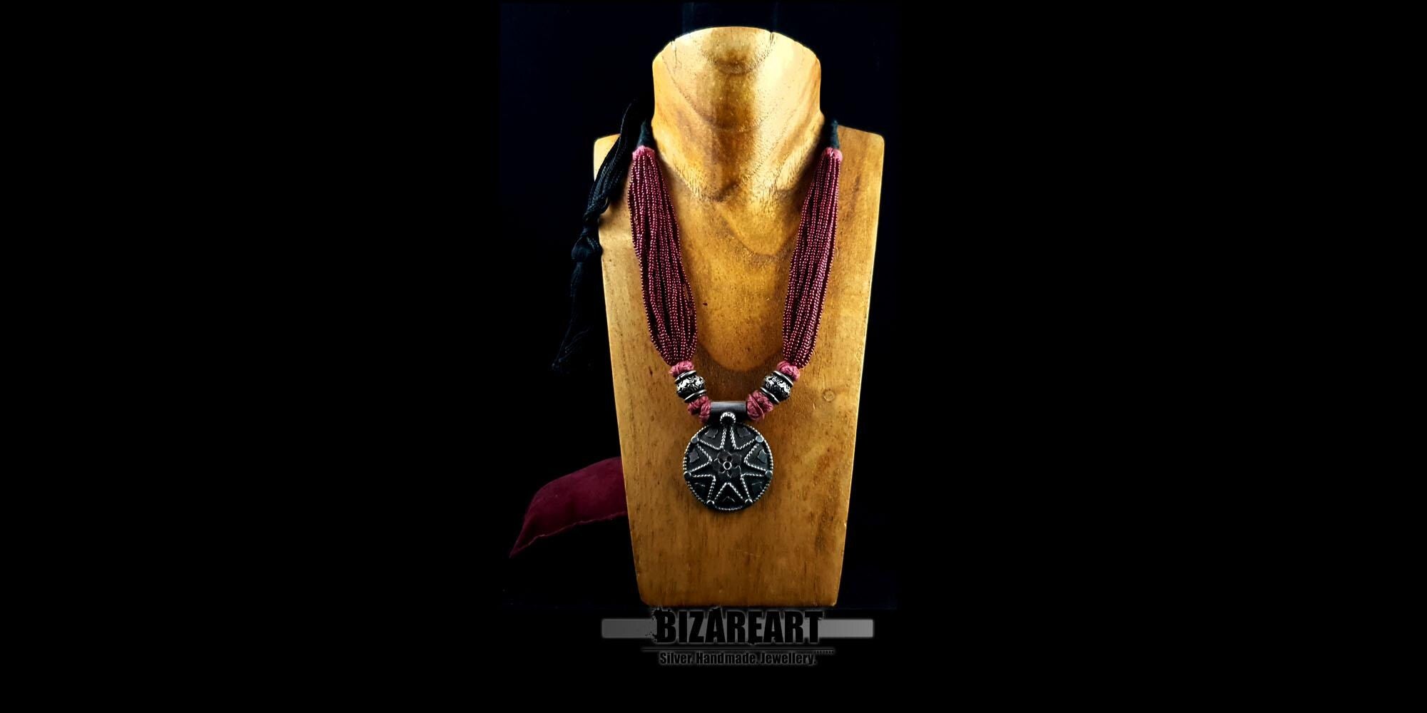 Side-angled view of the adjustable multi-strand red statement necklace on a wooden mannequin display, highlighting its drape and texture.