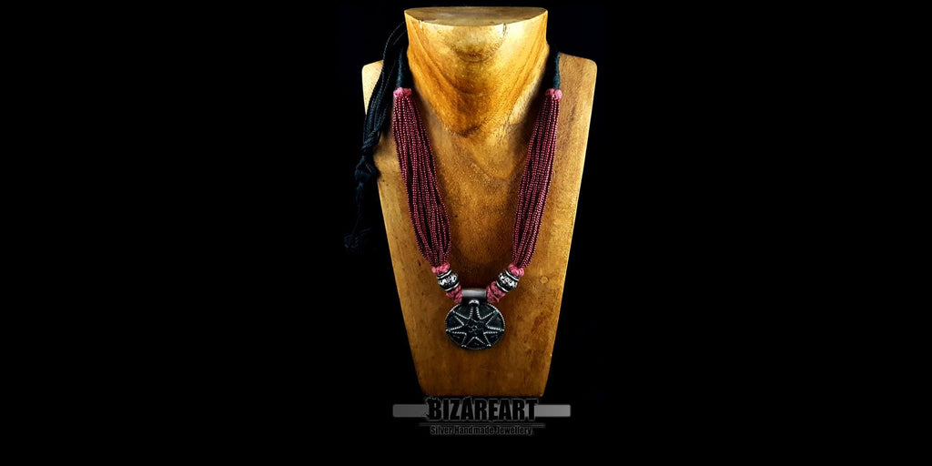 Front view of the red beaded tribal-style necklace with an ornate silver pendant, styled on a wooden bust mannequin against a black background.