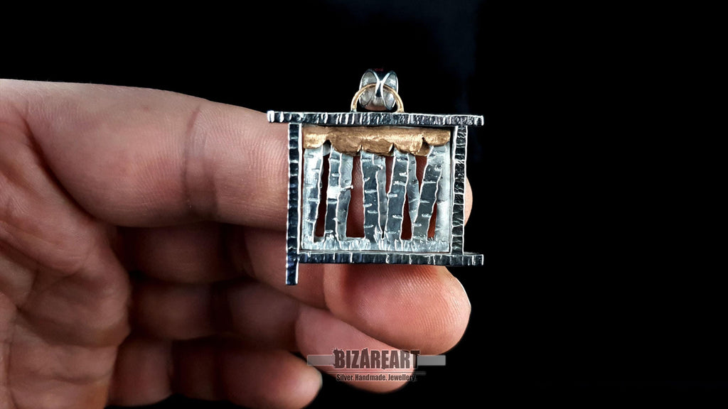 A person holding the silver forest pendant between two fingers to provide a clear scale reference of the 3.0 cm x 3.0 cm dimensions.