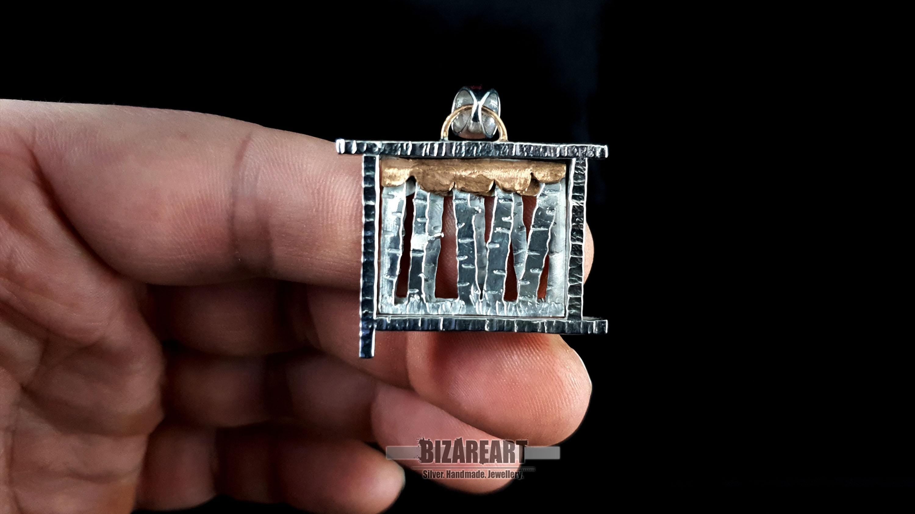 A person holding the silver forest pendant between two fingers to provide a clear scale reference of the 3.0 cm x 3.0 cm dimensions.