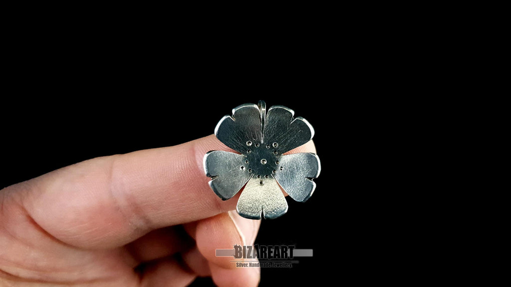 A person holding the 2.0 cm 925 sterling silver flower pendant between their fingers, showing the lightweight design and intricate drilled details.