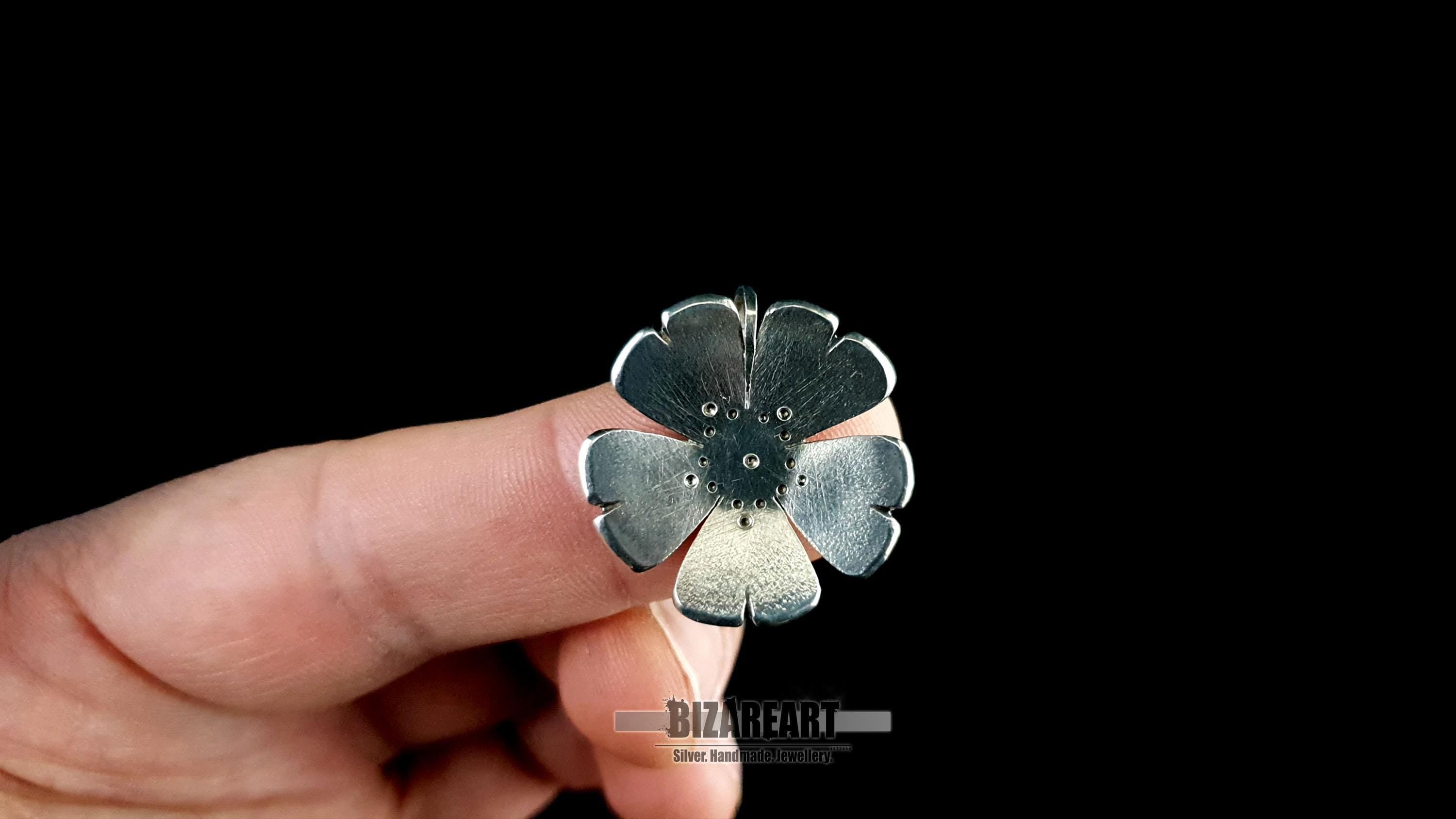 A person holding the 2.0 cm 925 sterling silver flower pendant between their fingers, showing the lightweight design and intricate drilled details.