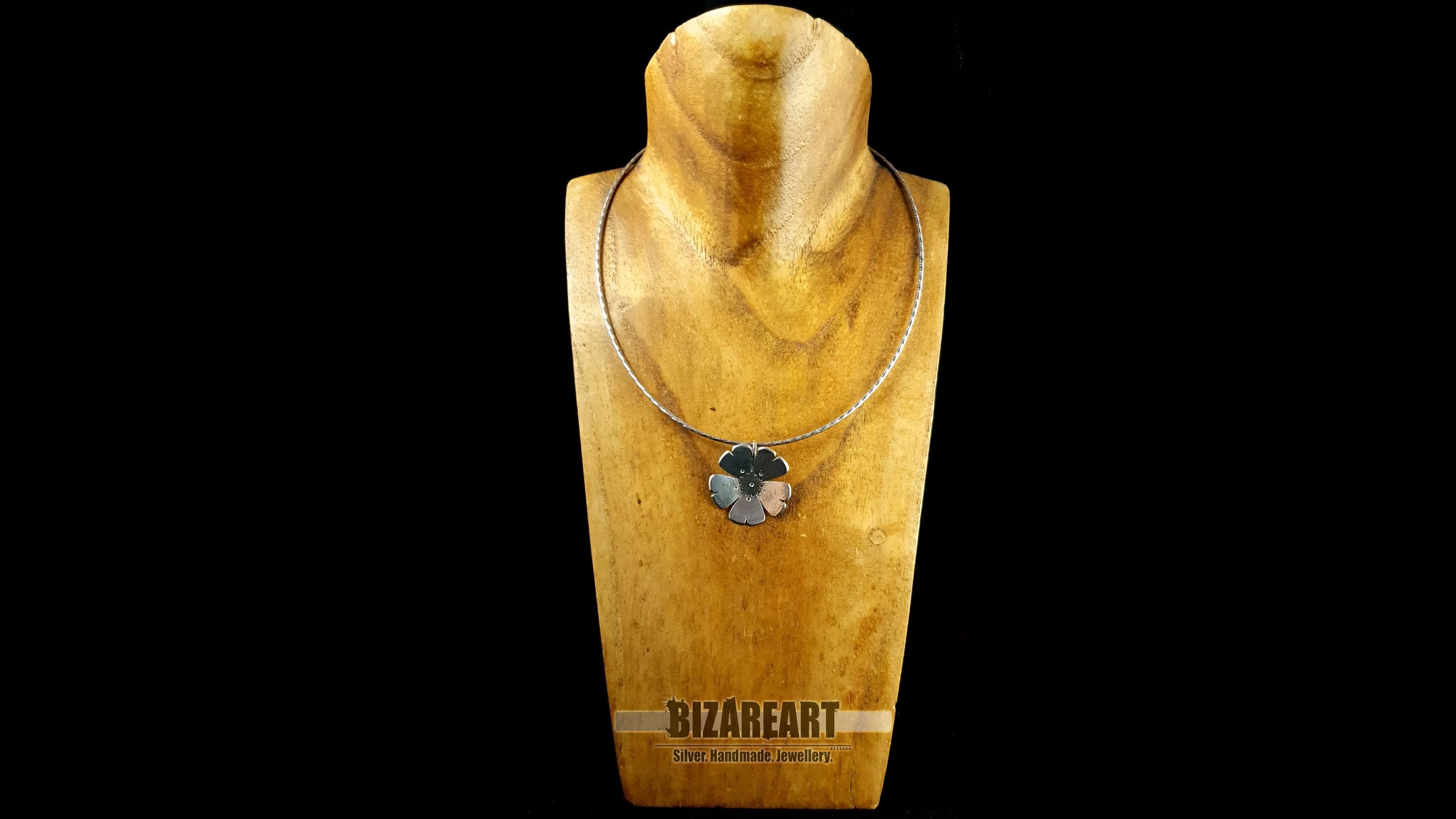 The rustic sterling silver flower pendant worn on a chain around a wooden neck mannequin to show scale and length.
