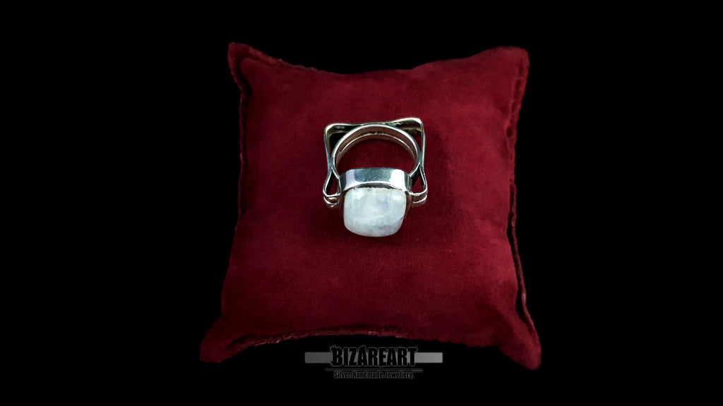 The silver moonstone ring resting on a plush red velvet cushion, emphasizing its status as a statement piece.