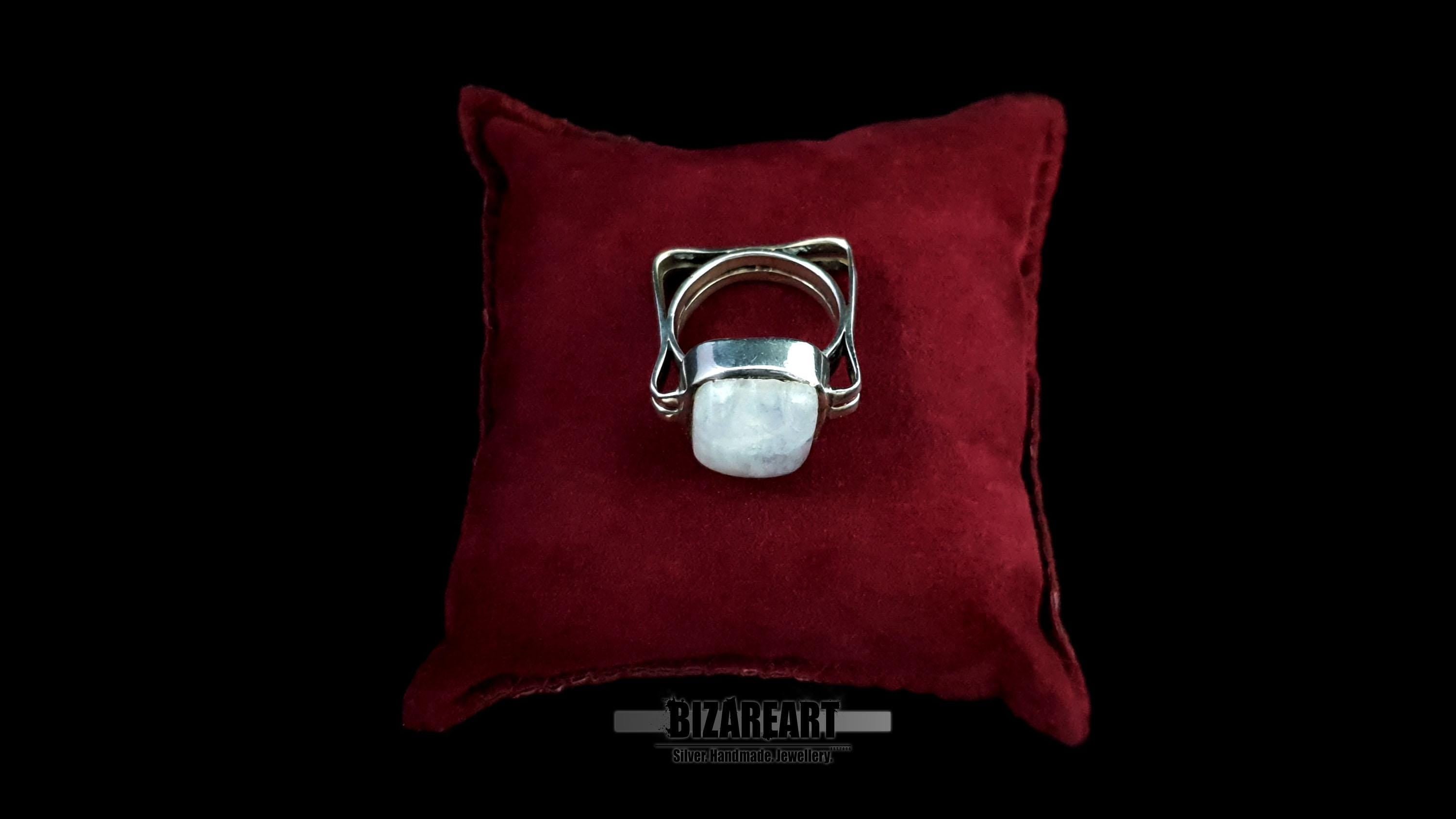 The silver moonstone ring resting on a plush red velvet cushion, emphasizing its status as a statement piece.
