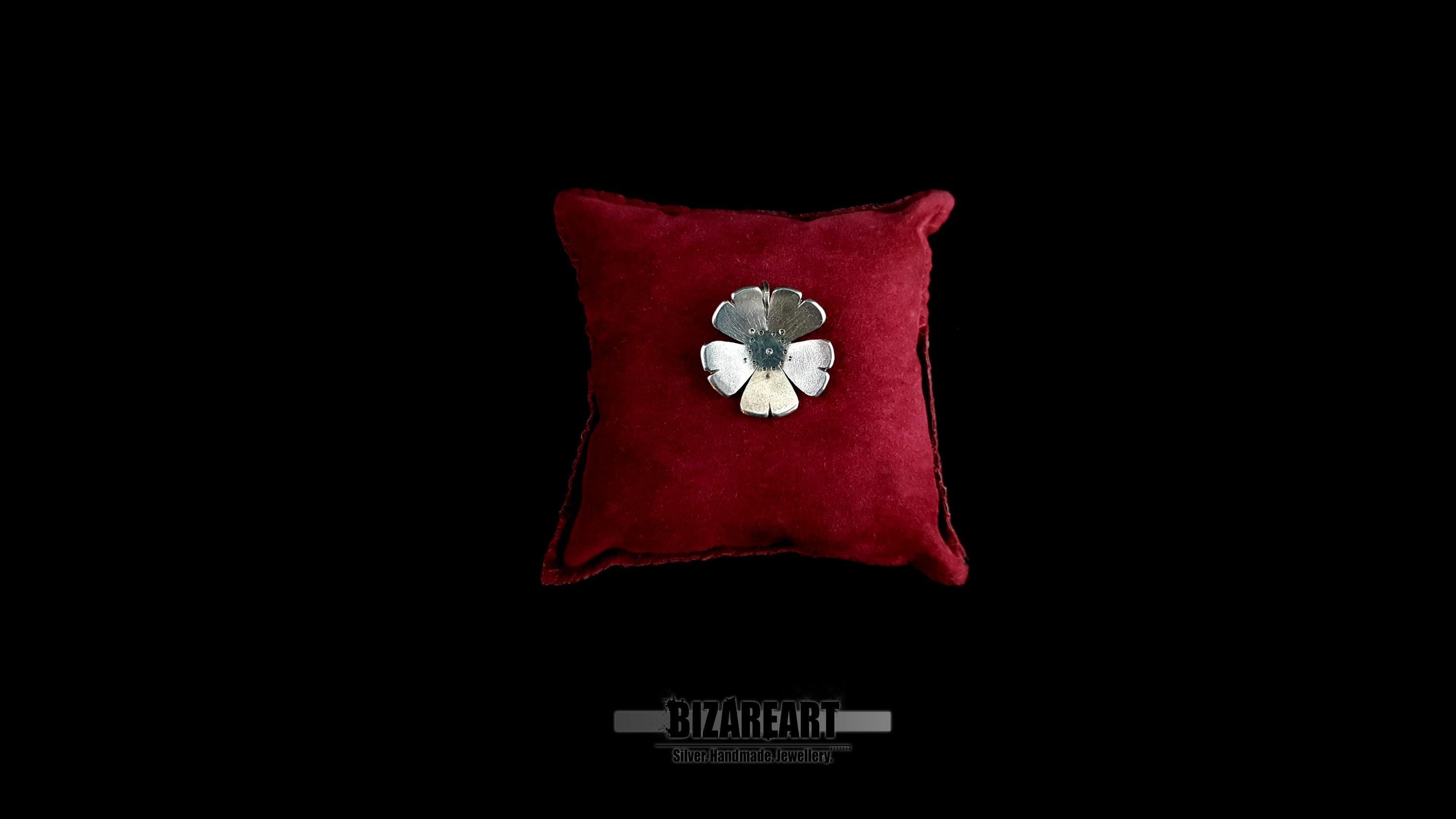 A handmade 925 sterling silver flower pendant with carved petals, displayed on a small red velvet cushion against a solid black background.