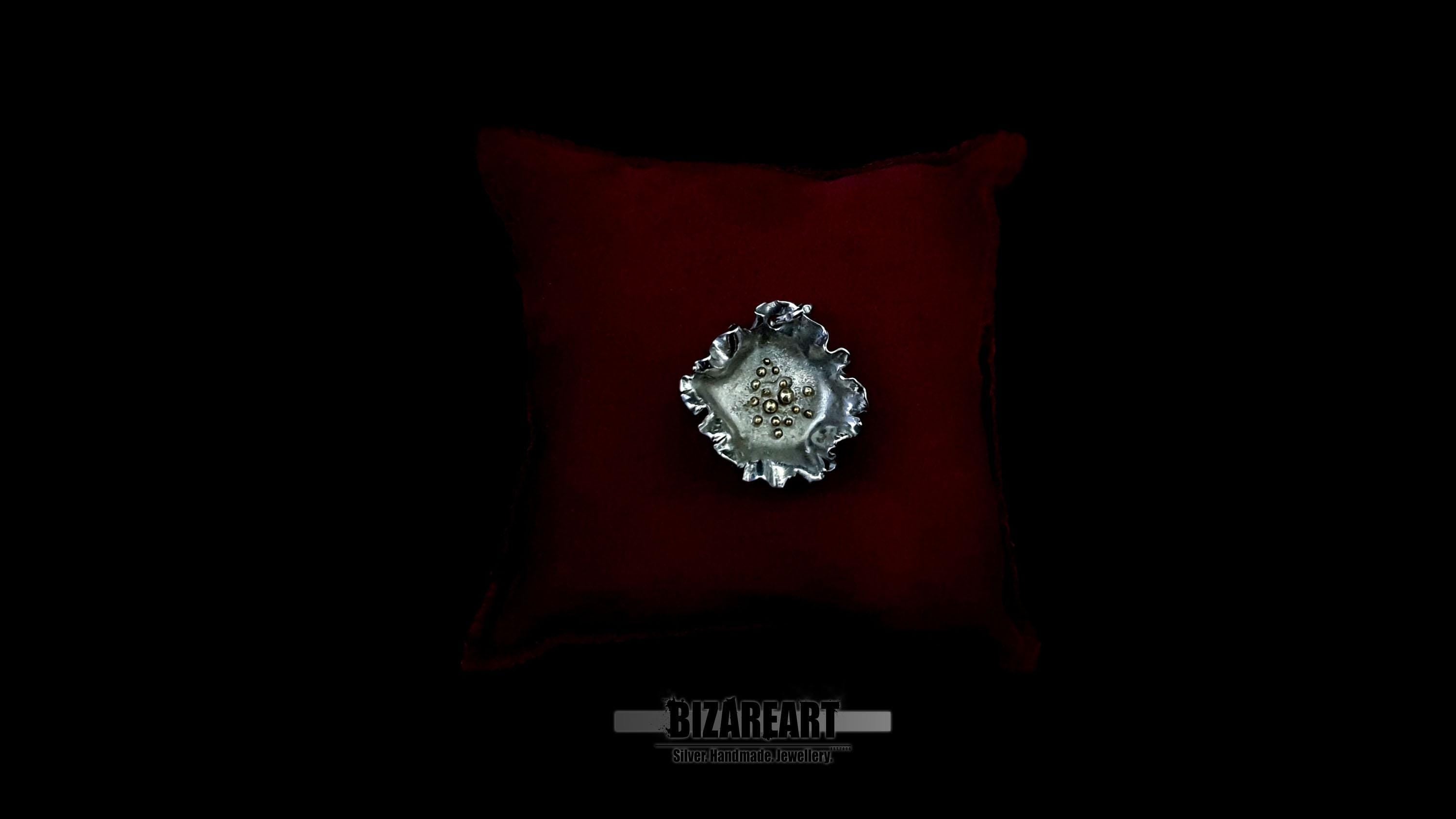 Close-up of an organic ruffled sterling silver pendant with gold center accents, resting on a dark red velvet pillow against a black background.