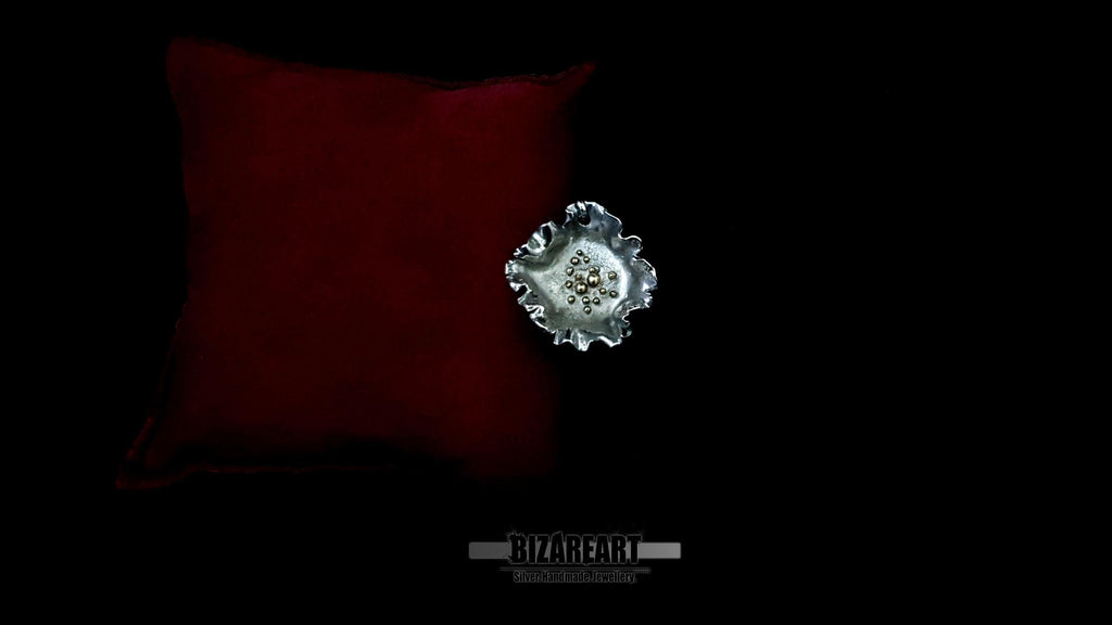 High-angle shot of the one-of-a-kind "Night Bloom" silver pendant displayed on a plush crimson cushion.