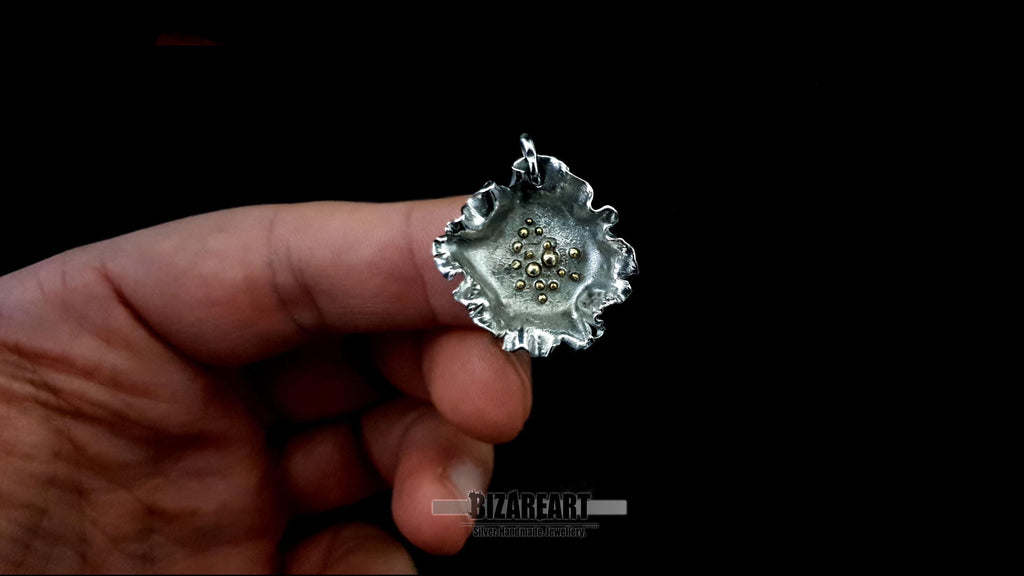 Close-up of a hand holding the silver pendant to demonstrate scale and the intricate, ruffled metallic texture.